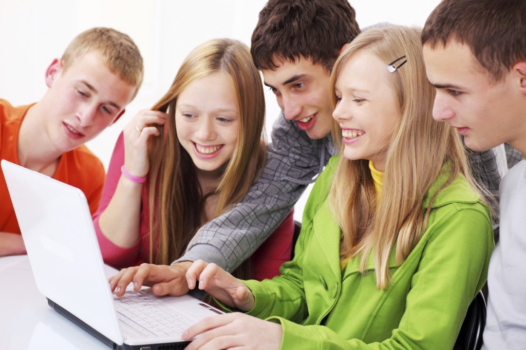 Smiling teens looking at laptop together.